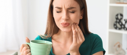 woman with a coffee mug touching her face due to a sensitive tooth